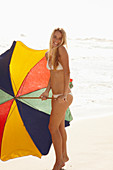 Blonde Frau mit Sonnenschirm in weißem Bikini am Strand
