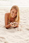 A blonde woman lying on a beach with shells