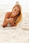 A blonde woman lying on a beach with shells