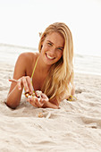 A blonde woman lying on a beach with shells