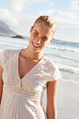 A blonde woman by the sea wearing a white embroidered dress