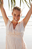 A blonde woman by the sea wearing a white embroidered dress