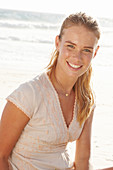 A blonde woman by the sea wearing a white embroidered dress