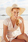 Blonde Frau mit Hut in weißem Kleid am Meer