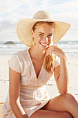 A blonde woman by the sea wearing a white dress and a hat