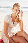 A blonde woman by the sea wearing a white embroidered dress