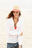 A brunette woman wearing a hat, a white blouse and denim shorts