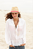 A brunette woman wearing a hat, a white blouse and denim shorts