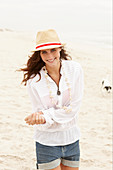 A brunette woman wearing a hat, a white blouse and denim shorts