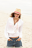 Brünette Frau mit Hut in weißer Bluse und Jeansshorts