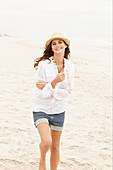 A brunette woman wearing a hat, a white blouse and denim shorts