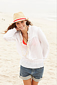 A brunette woman wearing a hat, a red bikini top, a white blouse and denim shorts