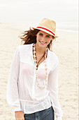 A brunette woman wearing a hat, a white blouse and denim shorts