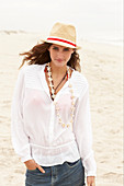 A brunette woman wearing a hat, a white blouse and denim shorts