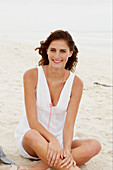 A brunette woman on a beach wearing a white summer dress