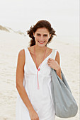 Brünette Frau in weißem Sommerkleid mit Tasche am Strand