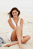 A brunette woman on a beach wearing a white summer dress