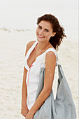 A brunette woman by the sea with a bag wearing a white summer dress