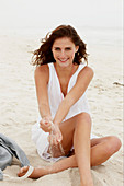 A brunette woman on a beach wearing a white summer dress