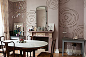 Dining table and fireplace in interior decorated with dusky pink wallpaper with abstract floral pattern