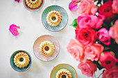 Mini vanilla Bundt cakes on a table next to a bouquet of roses