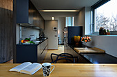 Blick in offene langgestreckte Küche mit dunkelblauen Küchenfronten und hellen Holzelementen