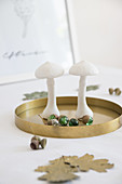 Autumnal arrangement of mushroom ornaments and acorns made from marbles on golden tray on table