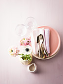 Napkins and cutlery on stacked plates with glasses and vase of flowers