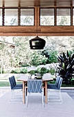 Wooden dining table with filigree metal chairs in front of a terrace