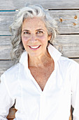 A mature woman wearing a white shirt standing against a wooden wall