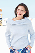 Junge Frau in hellblauem Pulli und bunter Hose am Strand