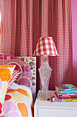 Colorful bed linen, bedside table and table lamp in front of a red and white checkered curtain in the girls' room