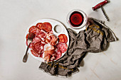 Antipasto meat platter assorti of sliced jamon, salami, chorizo sausage on white ceramic board with glass of red wine