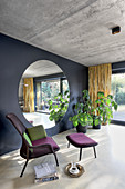 Armchair and footstool next to large round mirror on black wall