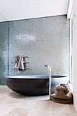 Black oval bathtub against a shimmering silver mosaic wall
