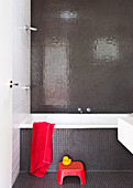 Bathroom with gray mosaic tiles, red stool in front of a bathtub