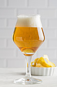 Glass of beer and chips on light background