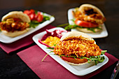 Appetizing burgers with tomatoes and crispy chicken on dark plates in gastrobar