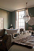 Frei stehende Badewanne im grünen Gästezimmer mit Kristallleuchter über Bett