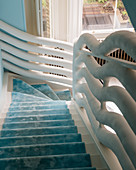 Staircase with sky-blue runner and white, sculptural balustrade