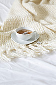 A cup of tea with teabag on a woollen blanket on a bed