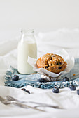 Blaubeermuffin und Milchflasche auf Stoffserviette im Bett