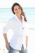 A brunette woman on a beach wearing a white shirt