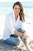 A brunette woman on a beach wearing a white shirt and jeans