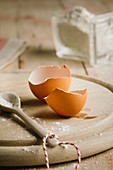 A egg shell on a wooden plate with a porcelain spoon
