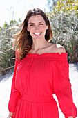 A brunette woman outside wearing a red off-the-shoulder dress