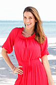 A brunette woman by the sea wearing a red dress