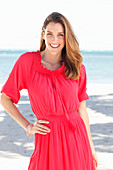 A brunette woman by the sea wearing a red dress