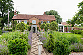 Gravel path flanked by flowerbeds leading to renovated English country house