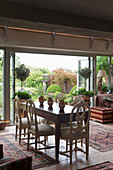 Dining table and antique chairs in front of open terrace doors in English country house